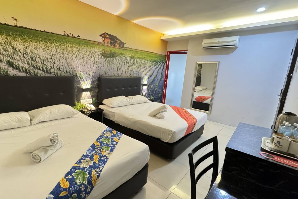 Una habitació d'hotel amb dos llits, un escriptori i un mural gran a la paret que representa un camp.
