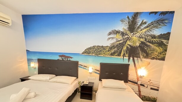 Habitación de hotel con dos camas, un mural grande con motivos playeros y una mesita de noche pequeña con un teléfono.