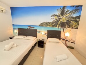 Habitación de hotel con dos camas, un mural grande con motivos playeros y una mesita de noche pequeña con un teléfono.