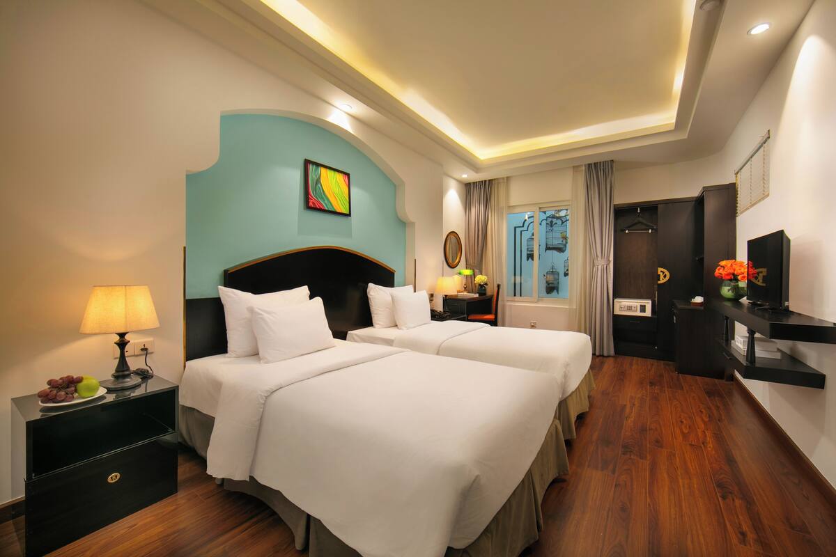 A hotel room with two beds, a desk, a TV, and a window with curtains.