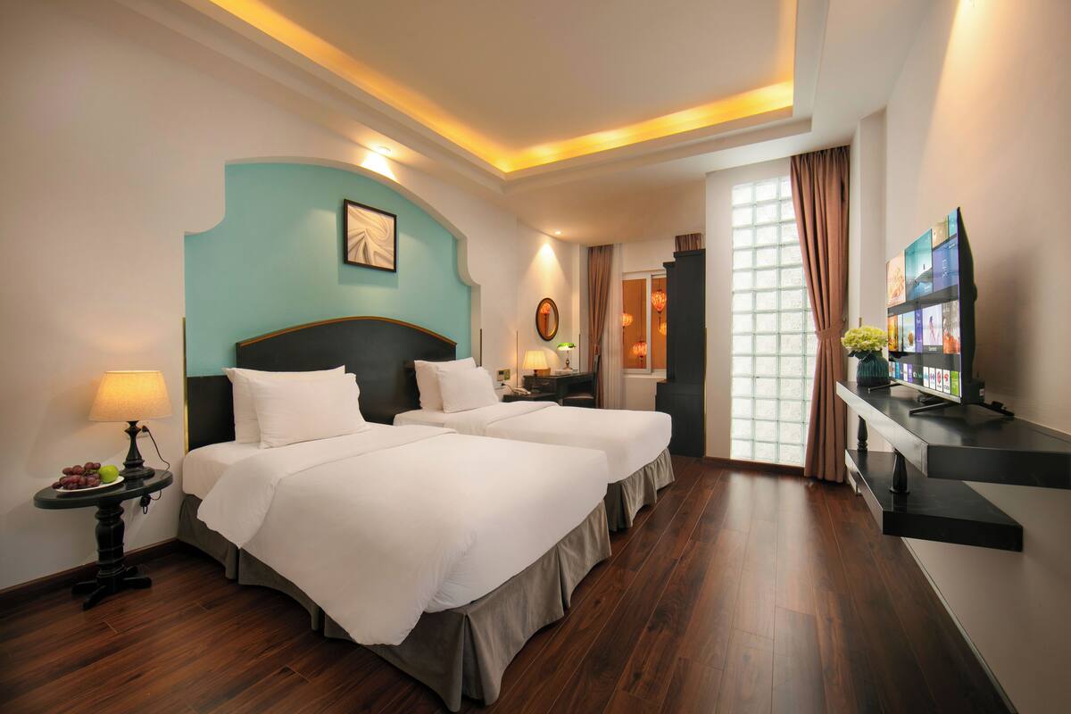 A hotel room with two beds, a desk, a TV, and a window with curtains.