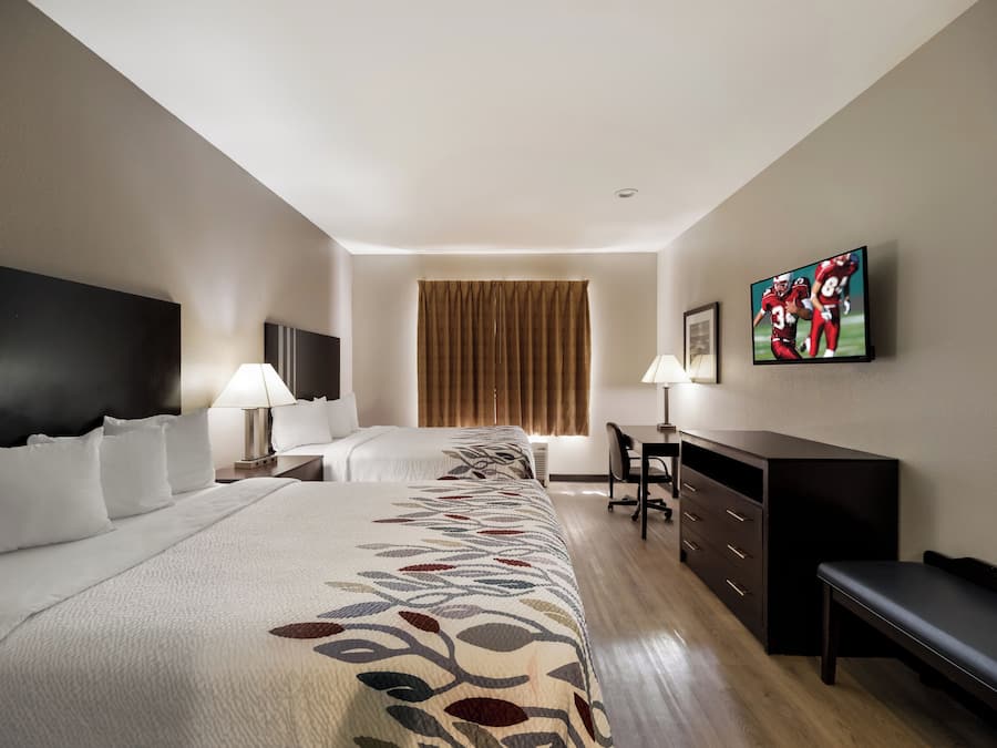 Hotelkamer met twee bedden, een bureau, een stoel, een televisie en een raam met gordijnen.