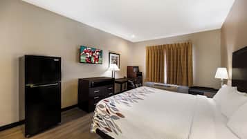 Habitación de hotel con cama, escritorio, silla, refrigerador, televisión y ventana con cortinas.