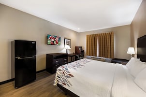 Habitación de hotel con cama, escritorio, silla, refrigerador, televisión y ventana con cortinas.