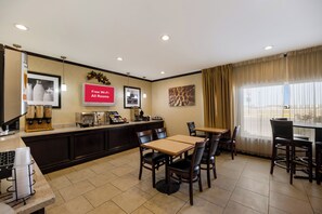 A hotel room with a kitchenette, a dining area with tables and chairs, a TV displaying 'Free Wi-Fi All Rooms', and a window with curtains.