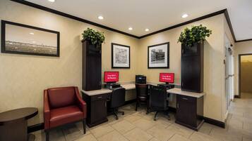 A hotel reception area with a red leather chair, two desks with computers, framed artwork on the walls, and a plant on top of a cabinet.