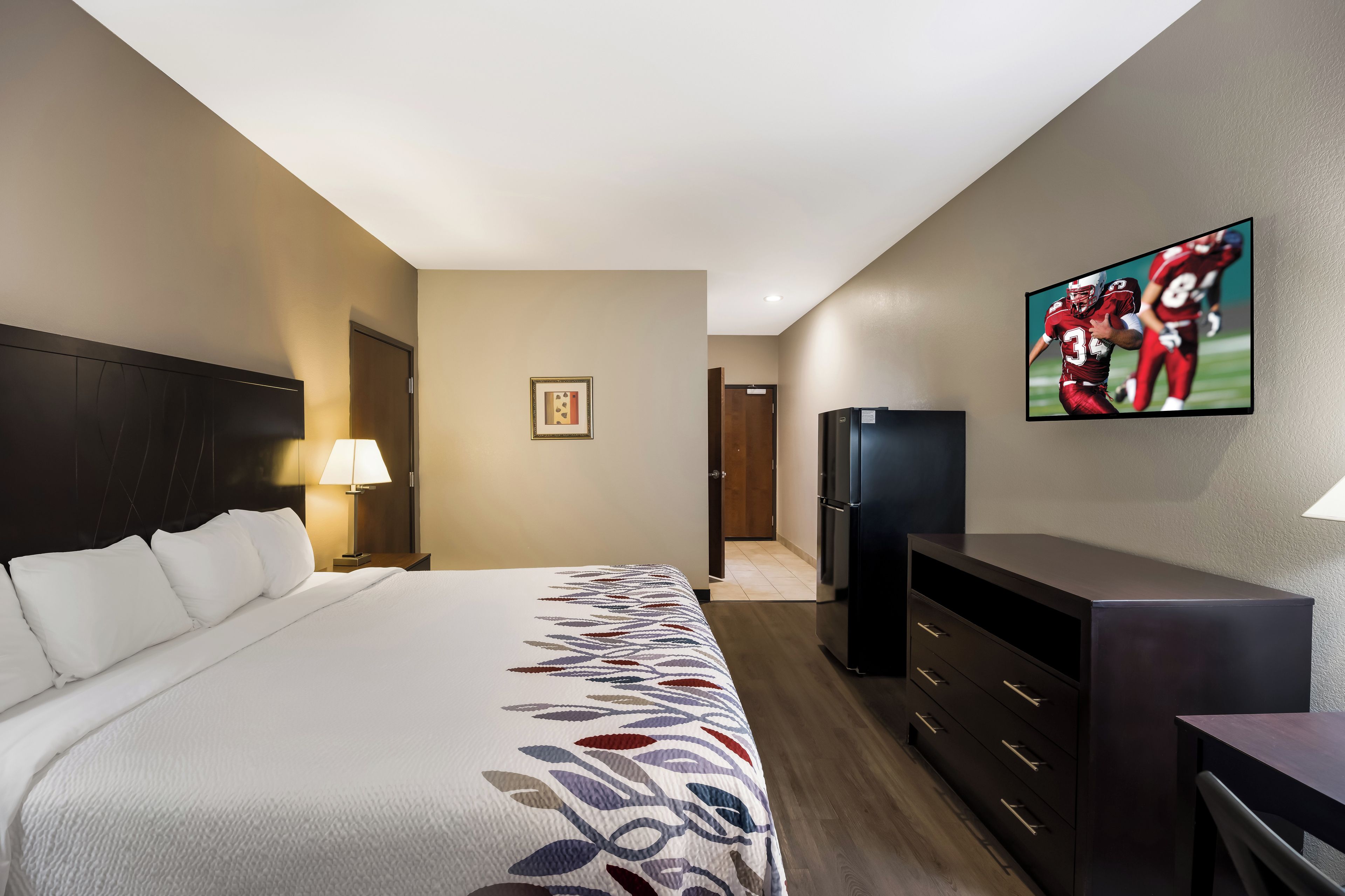 A hotel room with a bed, a TV, a refrigerator, and a desk.