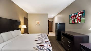 Una habitación de hotel con cama, televisión, refrigerador y escritorio.
