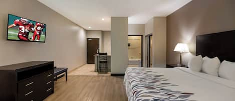 A hotel room with a bed, a desk, a chair, a TV on the wall, and a nightstand with a lamp.