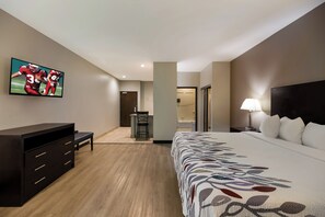 Een hotelkamer met een bed, een bureau, een stoel, een televisie aan de muur en een nachtkastje met een lamp.