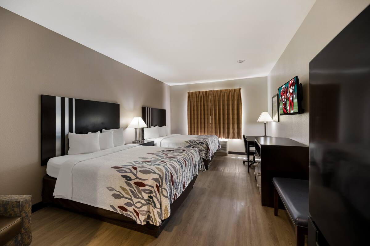 A hotel room with a large bed, a desk, a TV, and a window with curtains.