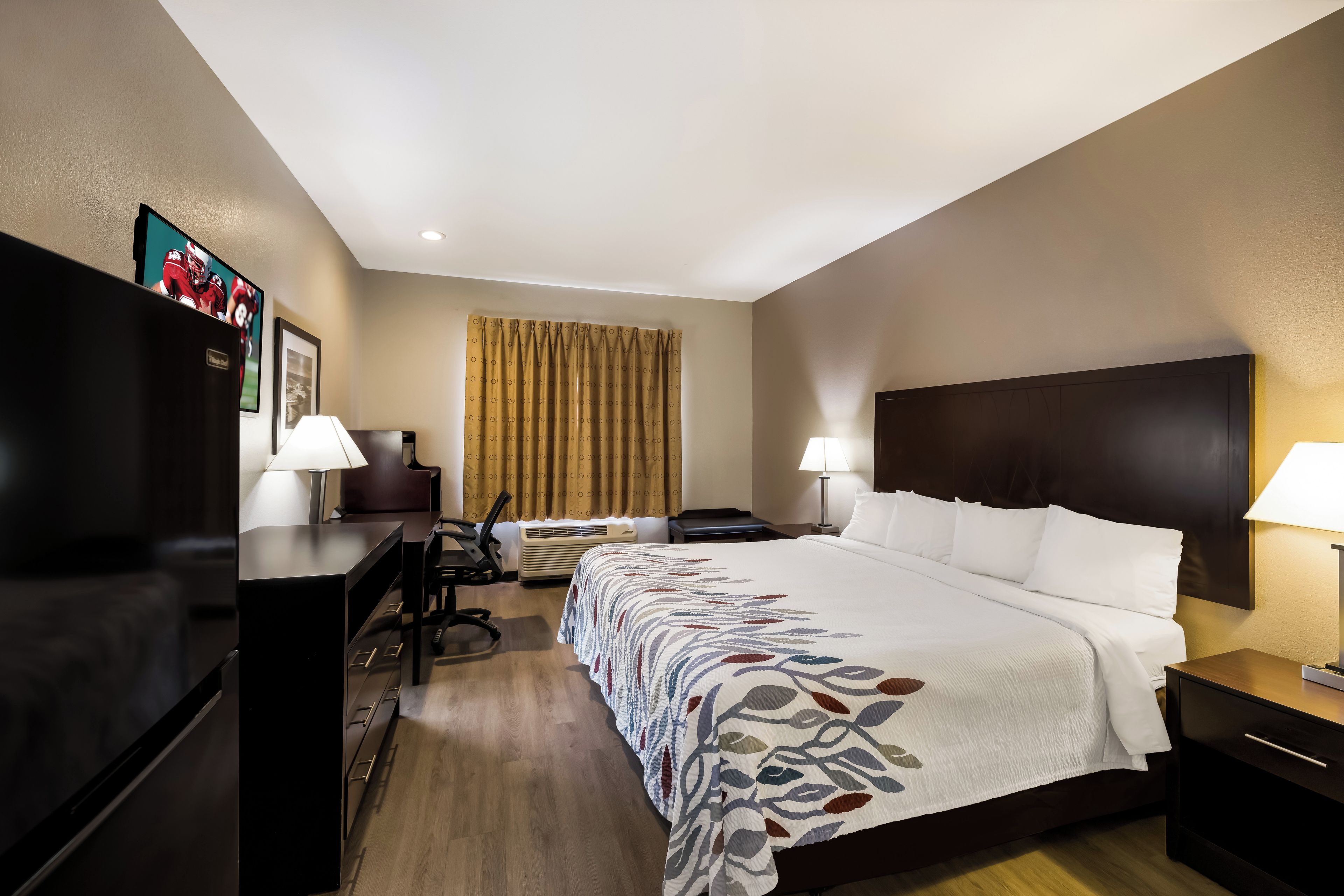 Habitación de hotel con cama, escritorio, silla, televisor y dos lámparas.