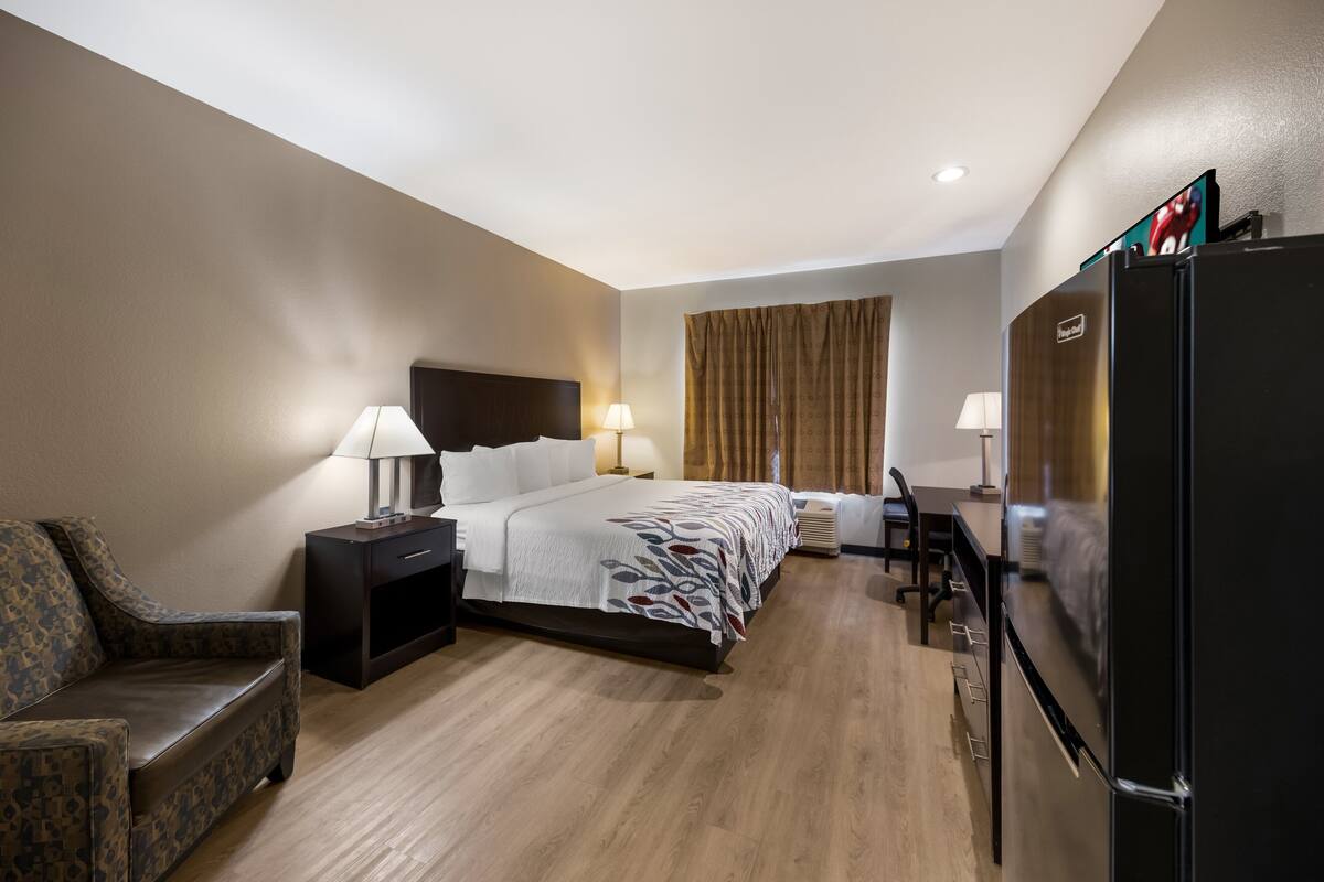 A hotel room with a bed, bedside tables, a desk, a chair, a refrigerator, and a television.