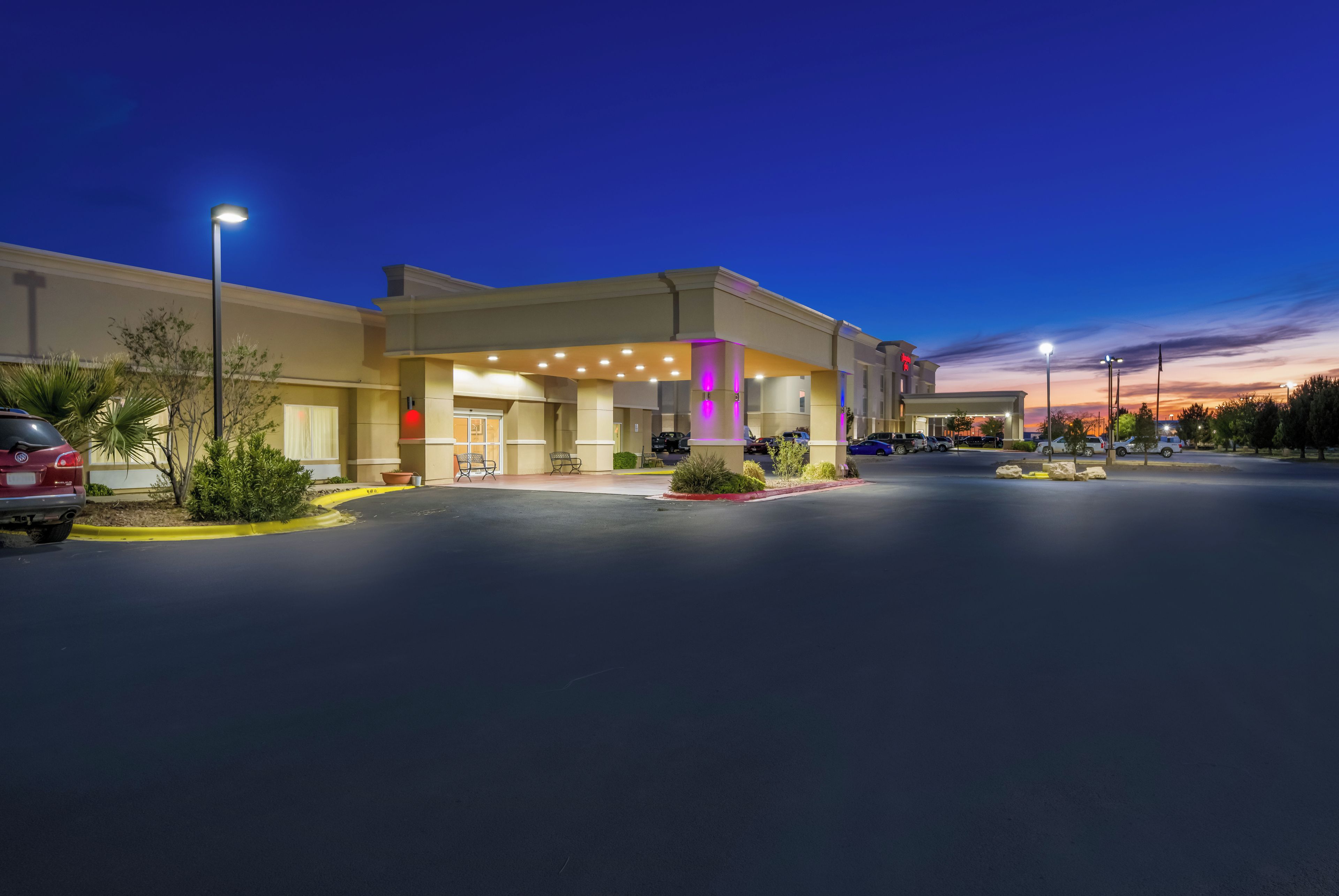 A hotel with a parking lot, a building entrance, and a clear sky.
