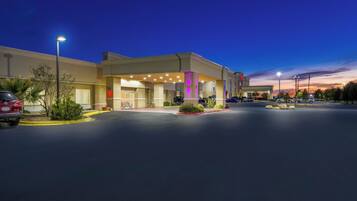 A hotel with a parking lot, a building entrance, and a clear sky.