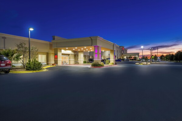 A hotel with a parking lot, a building entrance, and a clear sky.