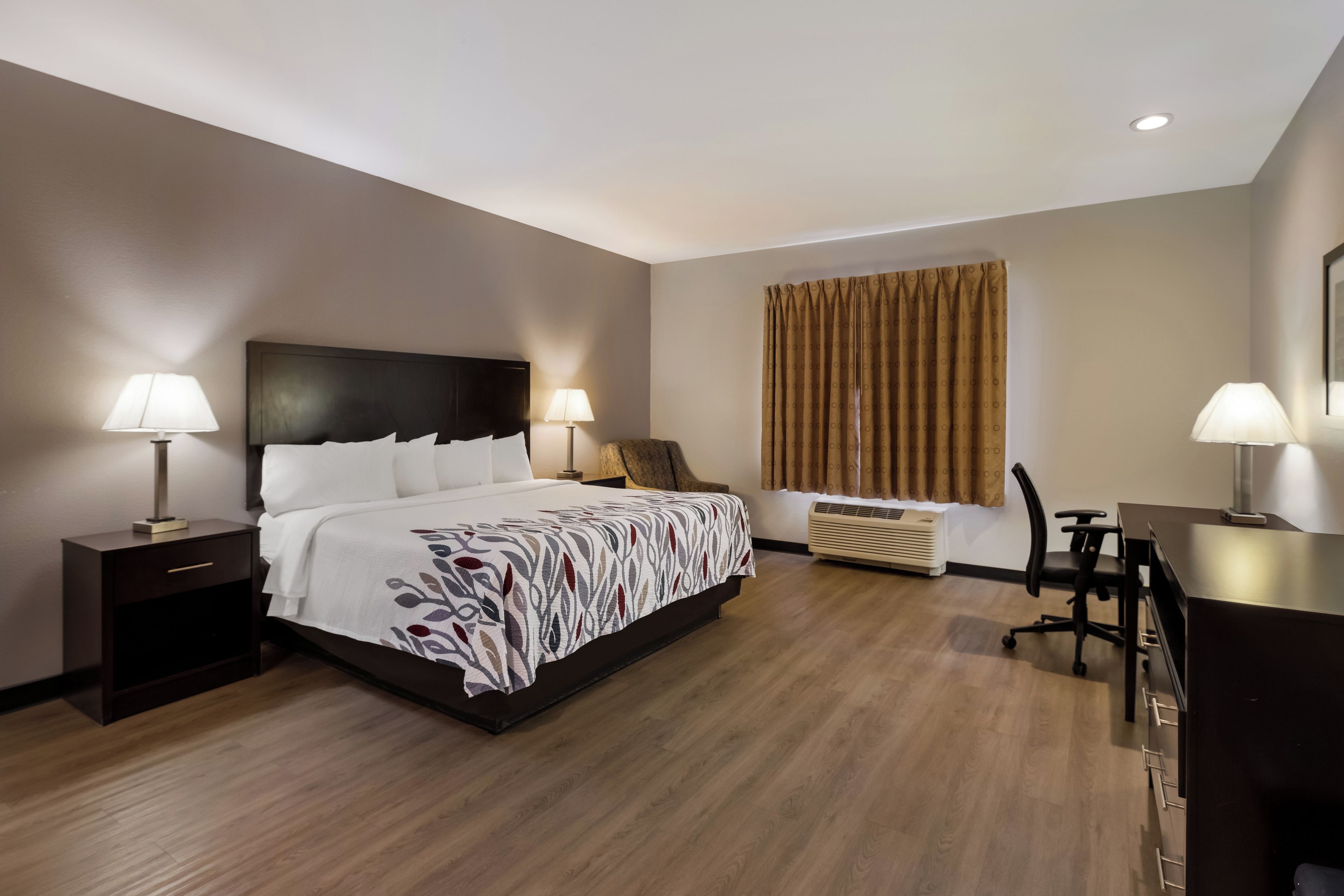 A hotel room with a bed, bedside tables, a desk, and a chair.