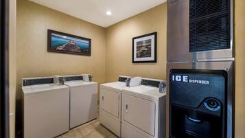 A laundry area with two washing machines, an ice dispenser, and two framed pictures on the wall.