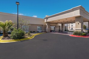 A hotel entrance with a covered waiting area, a parking lot, and landscaping.