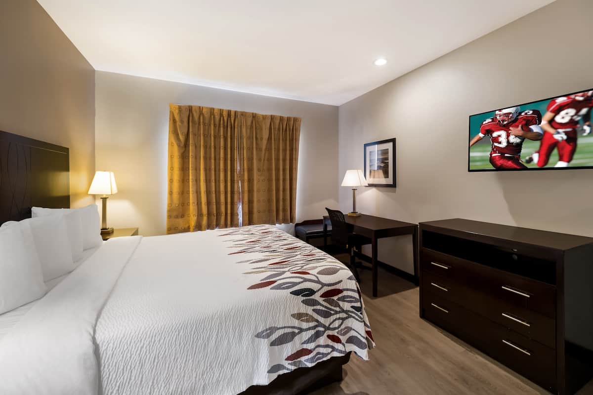 A hotel room with a large bed, a desk, a chair, a TV, and a wardrobe.
