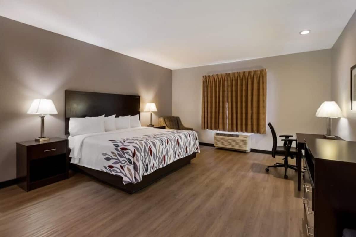 A hotel room with a bed, bedside lamps, a desk, and a chair.