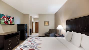 Una habitación de hotel con cama, televisión, escritorio con lámpara, silla y refrigerador.