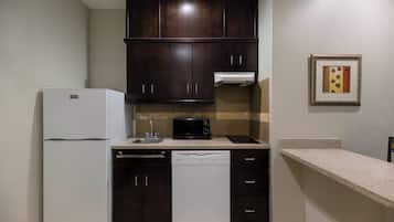 A compact kitchen with dark wooden cabinets, a white refrigerator, a dishwasher, a microwave, and a small countertop.