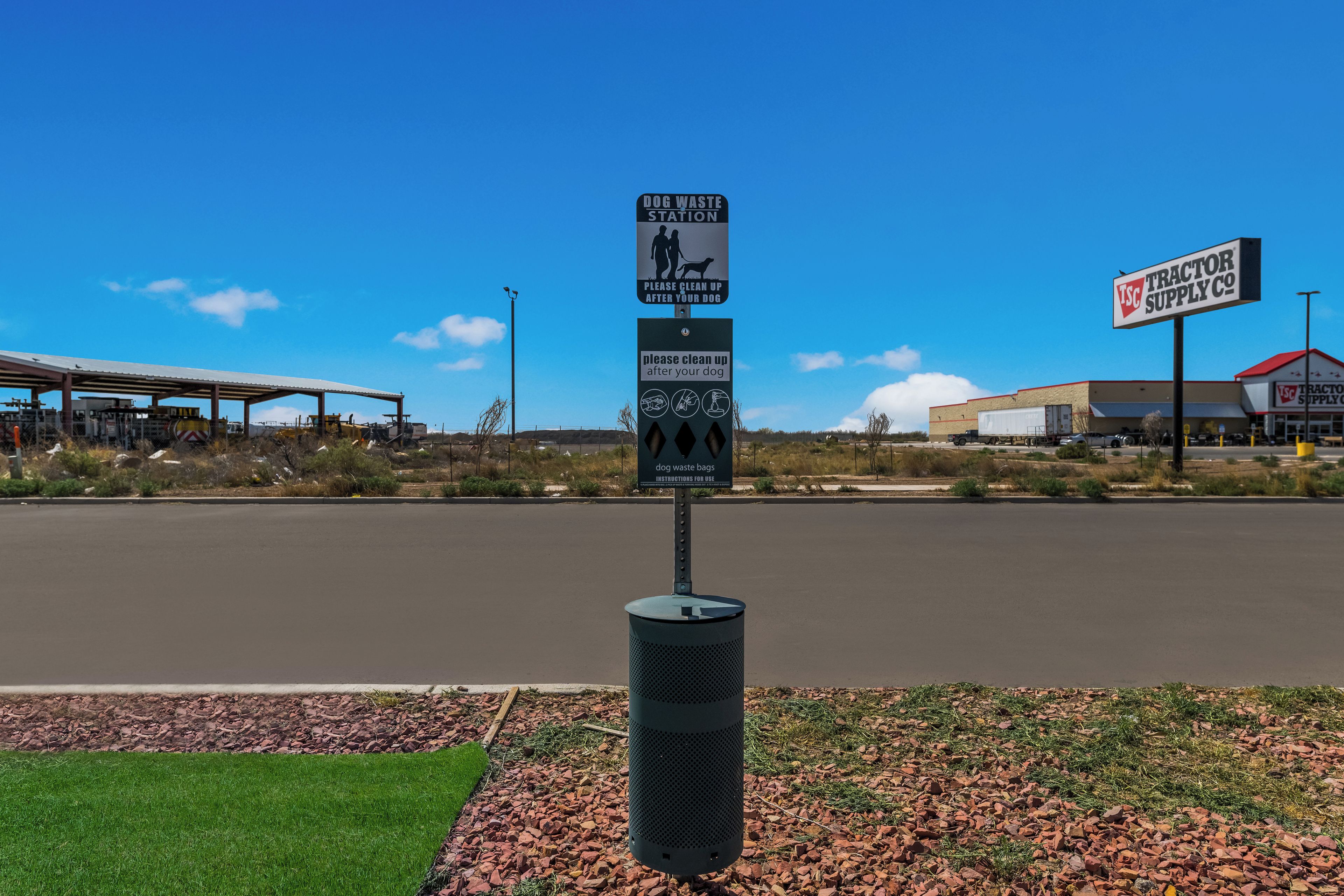 A dog waste station with a sign and a trash can in a parking lot.