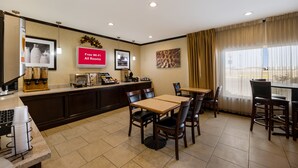 A hotel room with a kitchenette, a dining area with tables and chairs, a TV, and a large window with curtains. - Red Roof Inn Pecos (Pecos)