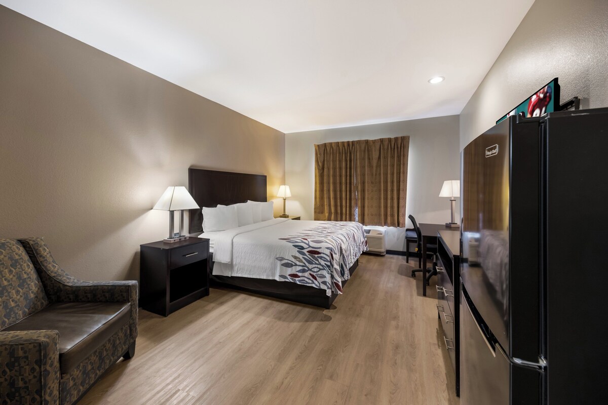 A hotel room with a bed, bedside tables, a desk, a chair, a refrigerator, and a television.