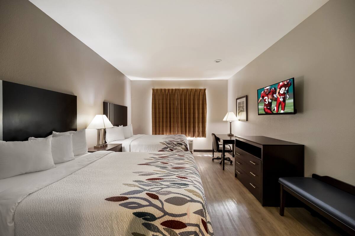 A hotel room with two beds, a desk, a chair, a TV, and a window with curtains.