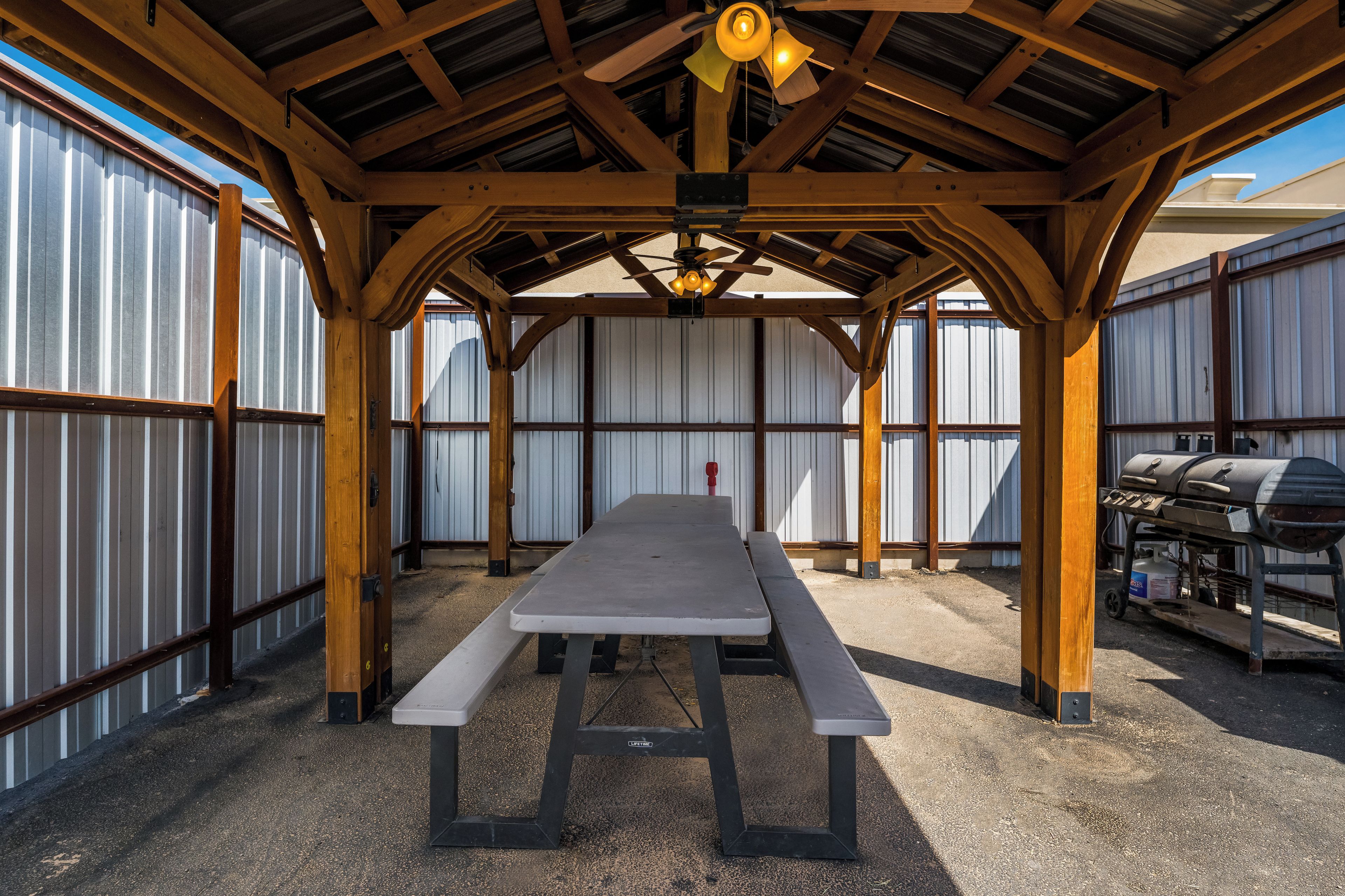 Un patio techado al aire libre con una mesa de picnic, cercado de metal y una parrilla.