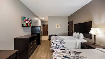 A hotel room with a bed, a desk, a television, a refrigerator, and a lamp.