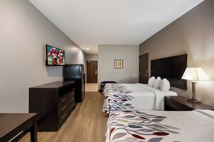 Una habitación de hotel con cama, escritorio, televisión, refrigerador y lámpara.