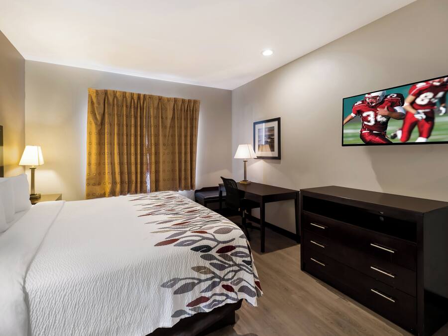 A hotel room with a bed, a desk, a chair, a TV, and a window with curtains.