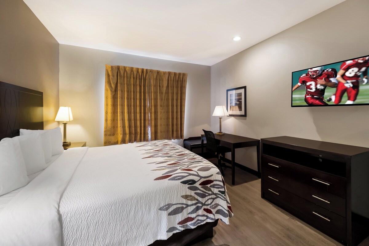 A hotel room with a large bed, a desk, a chair, a TV, and a wardrobe.