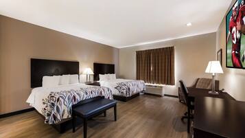 A hotel room with two beds, a desk, a chair, a TV, and a window with curtains.