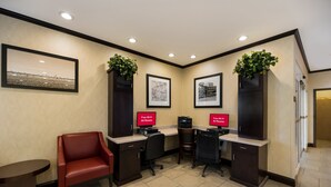 A reception area with a red chair, two desks with computers, framed pictures, and a plant. - Red Roof Inn Pecos (Pecos)