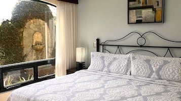 A bedroom with a bed, a window with curtains, a wall-mounted artwork, and a ceiling light fixture.
