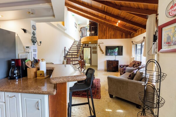 Una cocina amplia con una isla central, un comedor con sofá y sillas, y una escalera que conduce a un nivel superior.