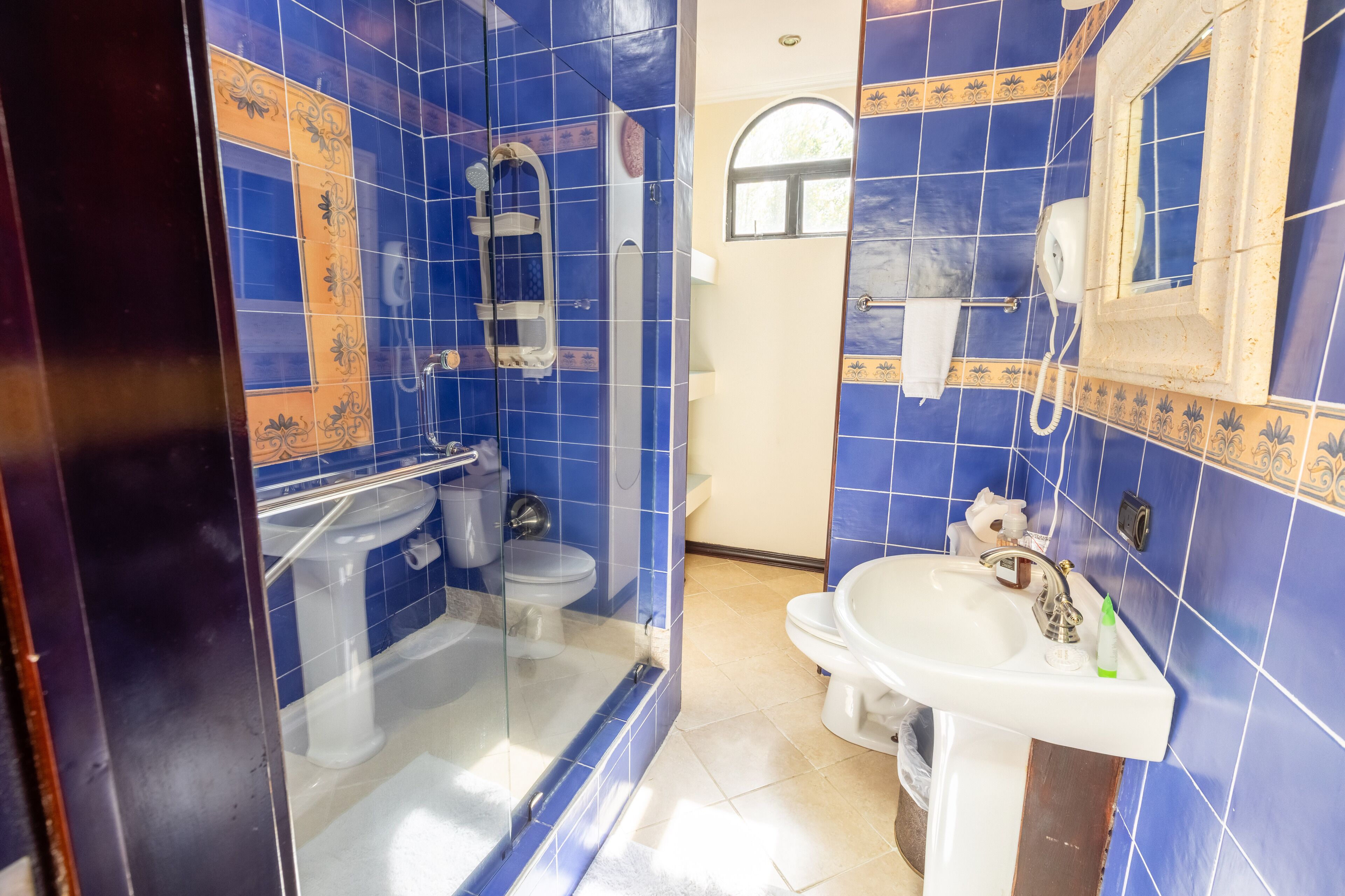 Une salle de bain avec des carreaux bleus, une douche en verre, un lavabo blanc et un miroir.
