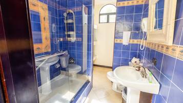 Une salle de bain avec des carreaux bleus, une douche en verre, un lavabo blanc et un miroir.
