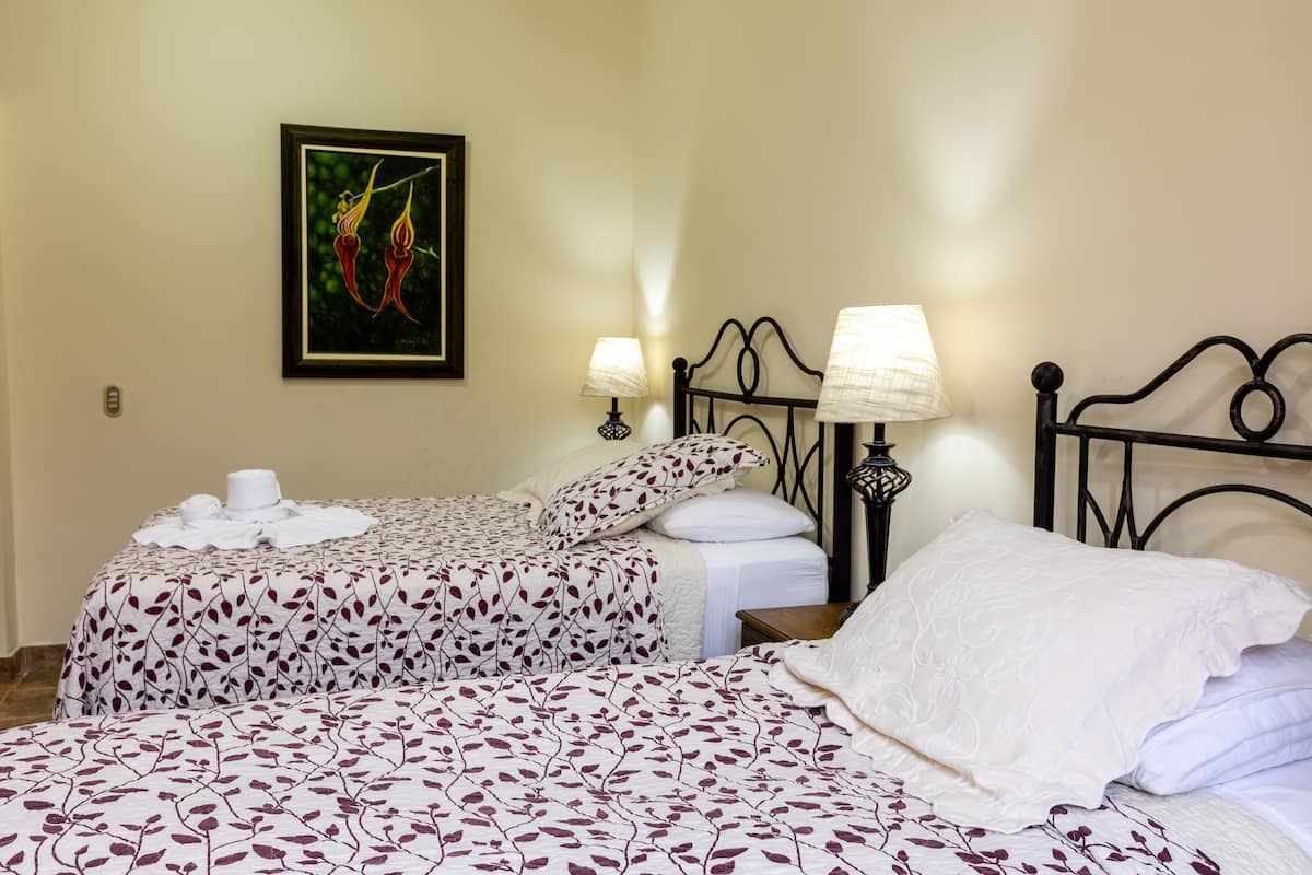 A hotel room with two beds, each with a patterned bedspread, a framed painting on the wall, and two bedside lamps.