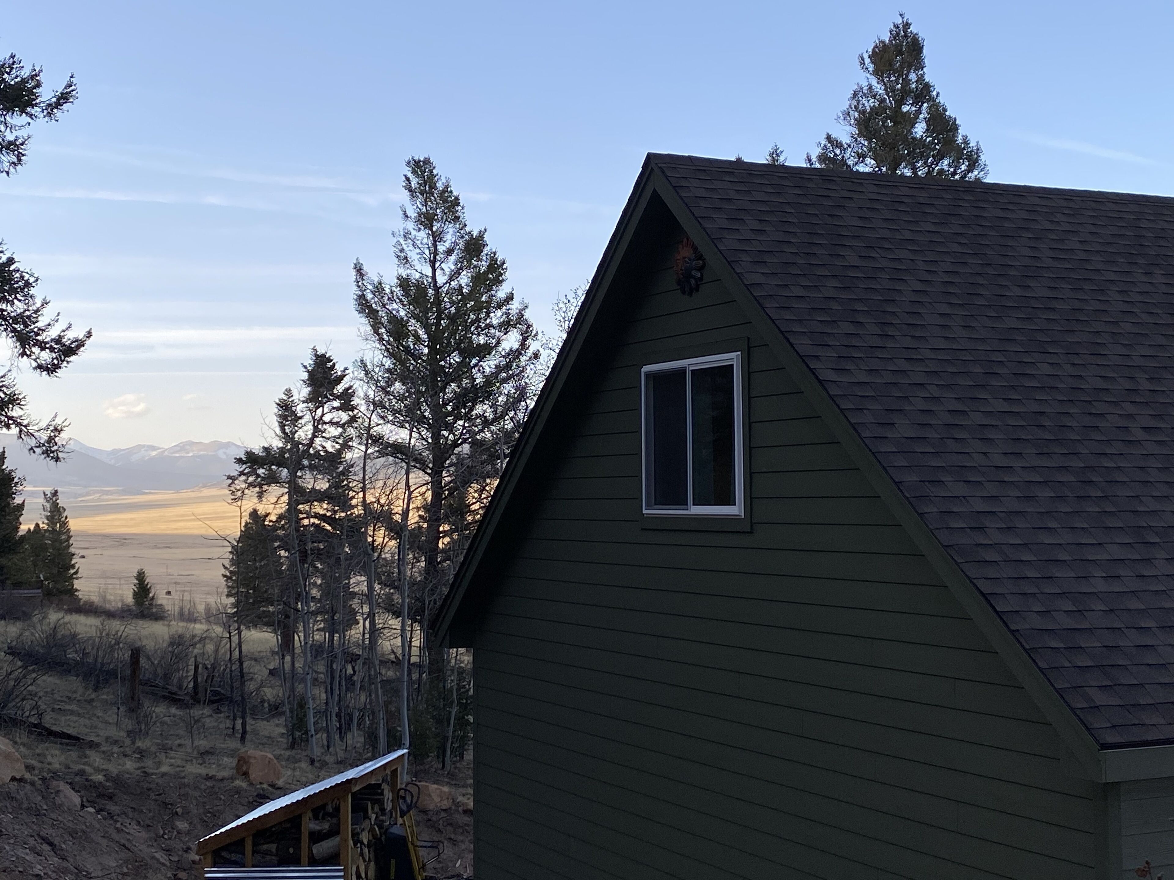 A green house with a dark roof, a window, and a view of mountains and trees.