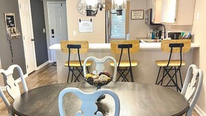 A dining area with a round table, four chairs, and a bowl of assorted pastries. There are two pendant lights above the table, a white countertop with a sink, and a sign that reads "GATHER TOGETHER." - 2 UNITS, Ground Floor, Branson's Pointe Royale, INDOOR POOL, Golf, Sleeps 12 (Branson)