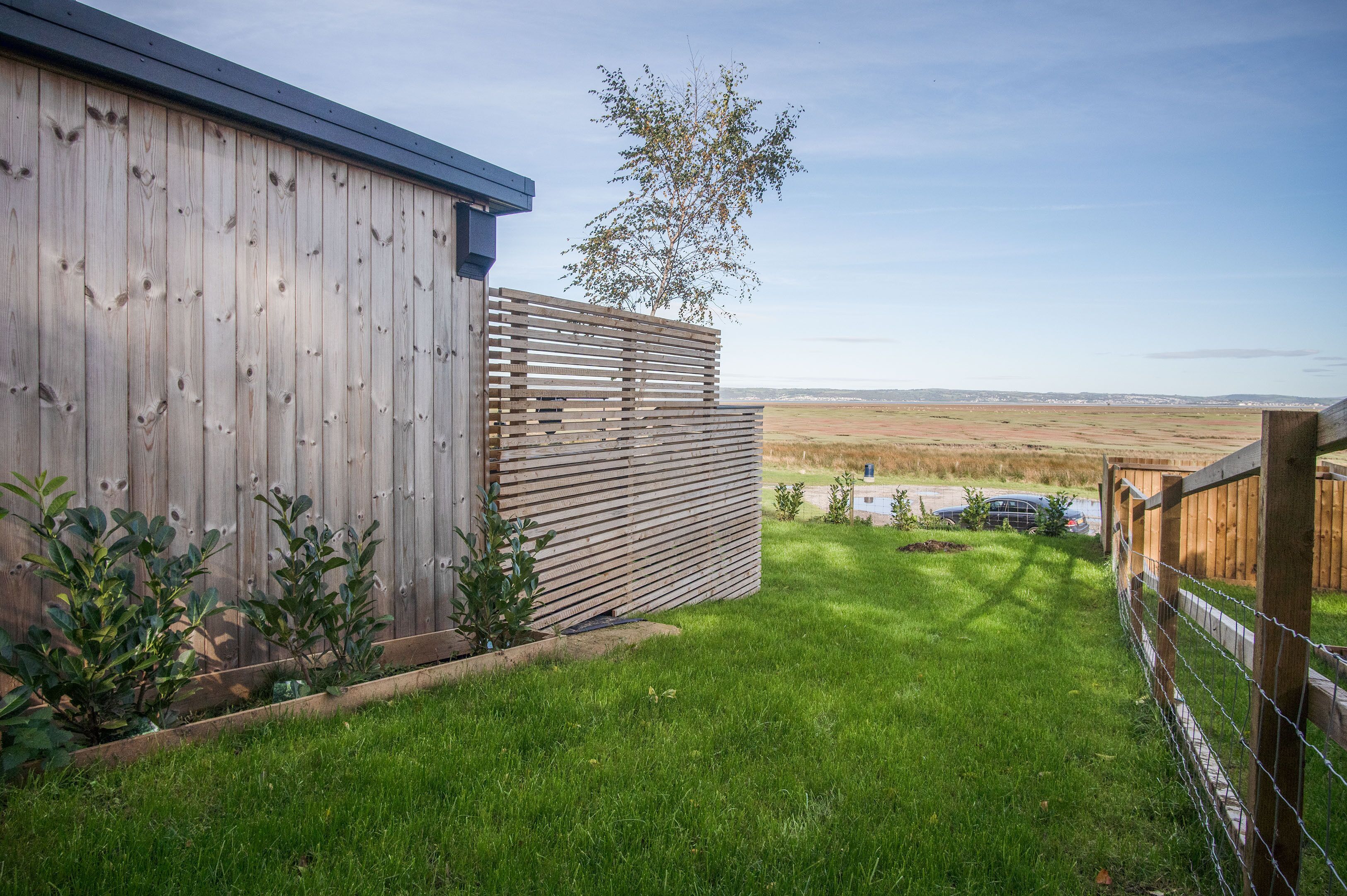 A wooden building with a slatted fence and a grassy yard.
