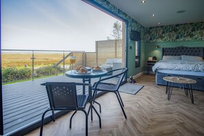 Un dormitorio con una cama grande, un balcón con mesa y sillas, y vistas al campo.