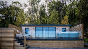 A modern wooden cabin with a glass enclosure, wooden stairs, and a view of the surrounding forest. - Caswell Bay Hide Out - Cabin - Landimore (Swansea)