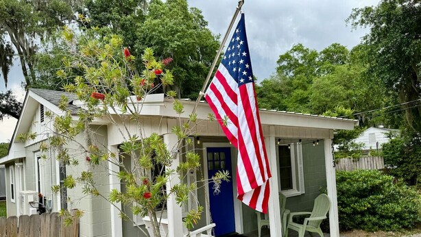 Een klein huis met een veranda, een Amerikaanse vlag en een blauwe deur.