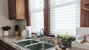 Una cocina con dos lavamanos de acero inoxidable, armarios de madera y un ventanal con persianas.